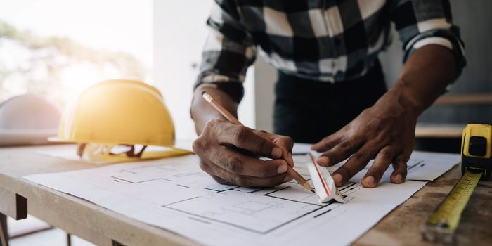 Image of engineer drawing a blue print design building or house, An engineer workplace with blueprints, pencil, protractor and safety helmet, Industry concept..