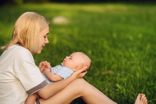 A mother holds a happy baby boy in her arms in a summer park.