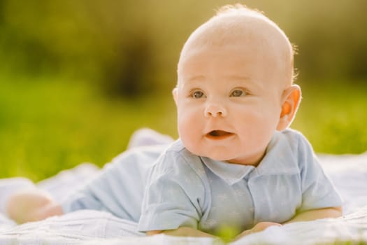 Cute happy toddler lying on a blanket on the grass outdoors in summer.