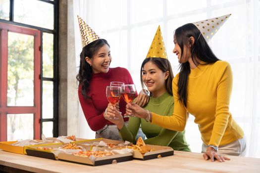 Group of Asian friends gather to celebrate Christmas with champagne and eating pizza at home. Joy of holiday party with friends or colleague concept.