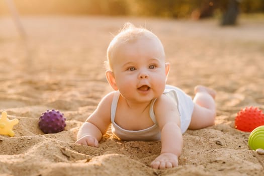 A happy little boy is lying on a sandy beach near the sea in the rays of the setting sun.