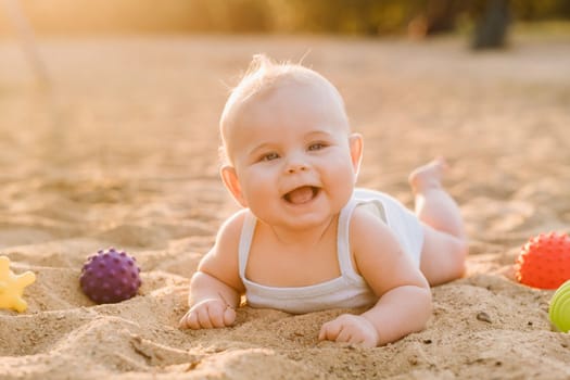 A happy little boy is lying on a sandy beach near the sea in the rays of the setting sun.