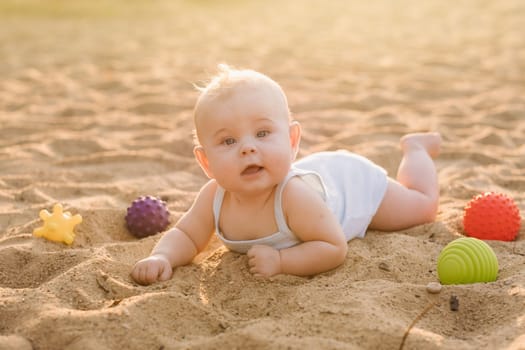 A happy little boy is lying on a sandy beach near the sea in the rays of the setting sun.