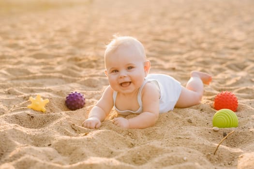 A happy little boy is lying on a sandy beach near the sea in the rays of the setting sun.