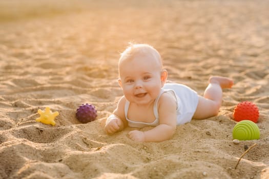 A happy little boy is lying on a sandy beach near the sea in the rays of the setting sun.