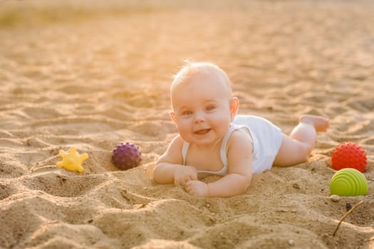 A happy little boy is lying on a sandy beach near the sea in the rays of the setting sun.