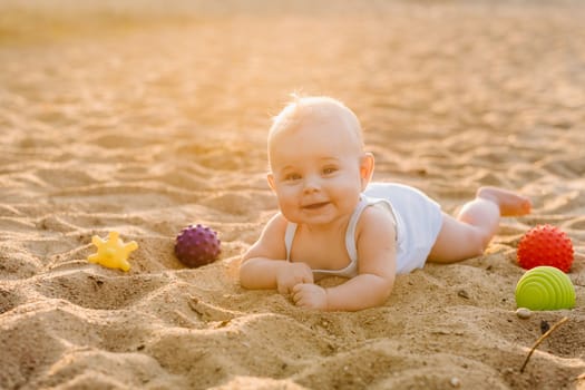 A happy little boy is lying on a sandy beach near the sea in the rays of the setting sun.