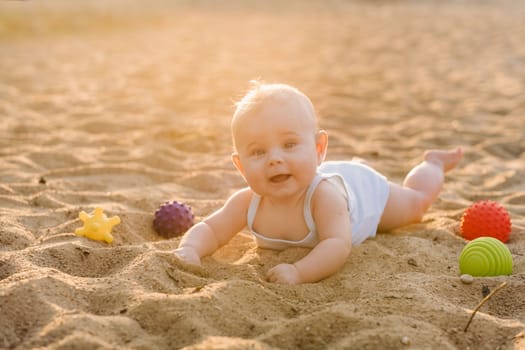 A happy little boy is lying on a sandy beach near the sea in the rays of the setting sun.