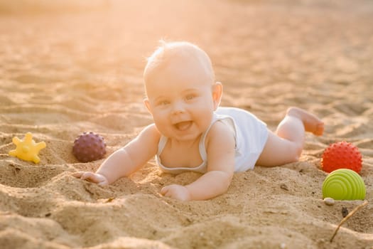 A happy little boy is lying on a sandy beach near the sea in the rays of the setting sun.