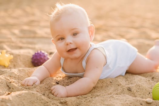 A happy little boy is lying on a sandy beach near the sea in the rays of the setting sun.