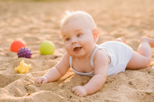 A happy little boy is lying on a sandy beach near the sea in the rays of the setting sun.