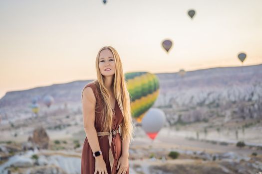 Tourist woman looking at hot air balloons in Cappadocia, Turkey. Happy Travel in Turkey concept. Woman on a mountain top enjoying wonderful view.
