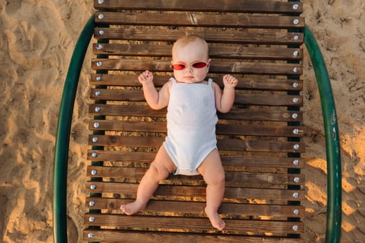 Top view of a happy little boy with glasses lying on a wooden sunbed.