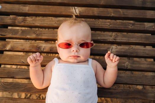 Top view of a happy little boy with glasses lying on a wooden sunbed.