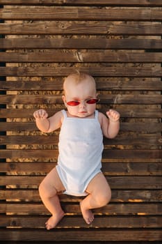 Top view of a happy little boy with glasses lying on a wooden sunbed.