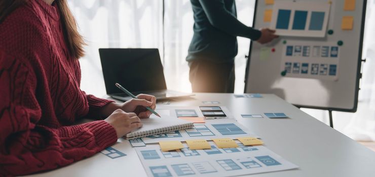 Ux developer and ui designer brainstorming about mobile app interface wireframe design on table with customer breif and color code at modern office.