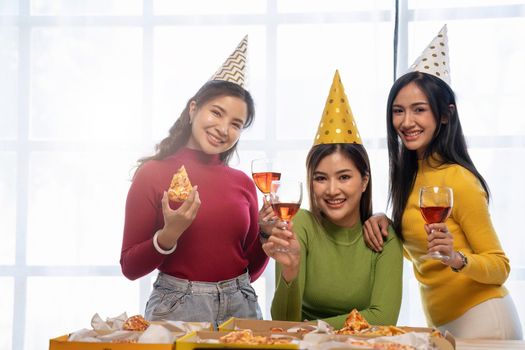 Group of Asian friends gather to celebrate Christmas with champagne and eating pizza at home. Joy of holiday party with friends or colleague concept.