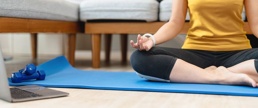 Crop of woman doing yoga exercise indoors at home, meditating. Self-isolation is beneficial, entertainment and education on the Internet. Healthy lifestyle concept.