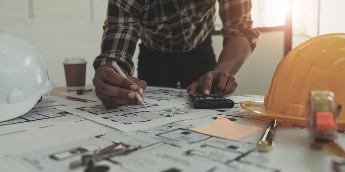 Image of engineer drawing a blue print design building or house, An engineer workplace with blueprints, pencil, protractor and safety helmet, Industry concept..