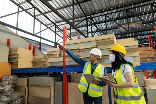 Two smile warehouse workers in uniforms and yellow helmets on heads standing and talking about job. adviser