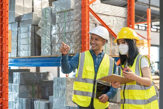 Two smile warehouse workers in white uniforms and yellow helmets on heads standing and talking about job.