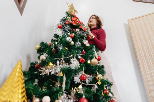 Decorating a Christmas tree. Young woman decorate the Christmas tree in living room at cozy home.