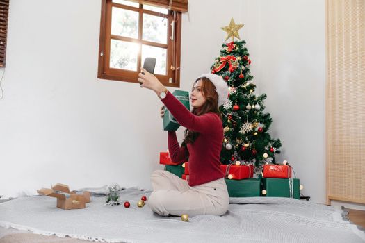 Holiday selfie at Christmas tree. Happy young girl taking selfie on smart phone at decorated Christmas tree iat home.