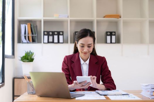 Asian Business woman using calculator and laptop for doing math finance on an office desk, tax, report, accounting, statistics, and analytical research concept.