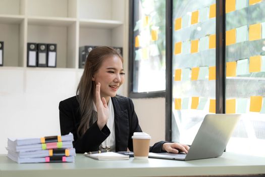 Beautiful Asian businesswoman is on video call with customer on laptop in office and has a negotiating gesture. smiling and happy face