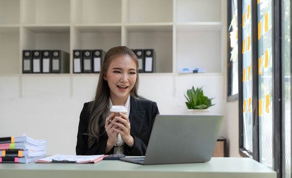 Pretty Asian businesswoman sitting on a laptop And the work came out successfully and the goal was achieved, happy and satisfied with her...
