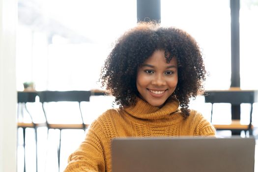 Photo of cheerful joyful mixed race woman in yellow shirt smiling work on laptop talk speak video call online. Smart ethnic female in earphones study distant on computer at home. Education concept...