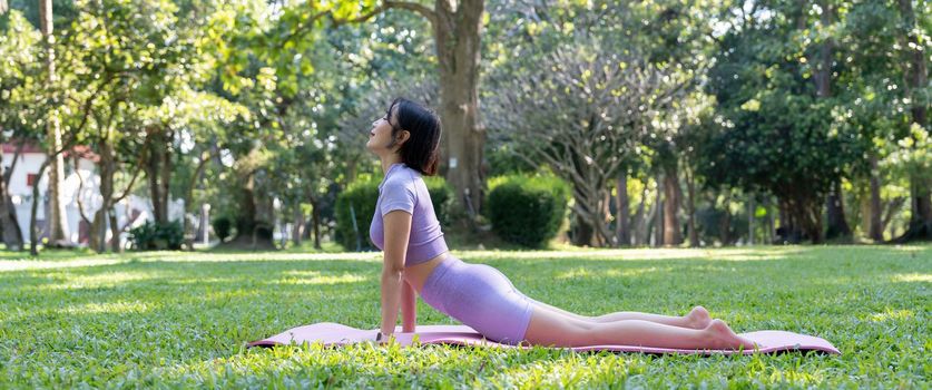 Mature healthy people doing yoga at park. Asian woman exercising on green grass with yoga mat