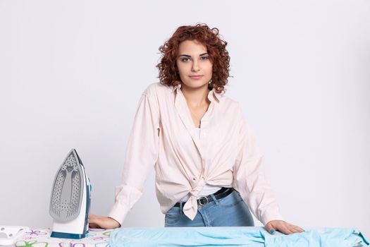 A girl with curly hair and a gentle smile on her face ready to start the daily ritual of ironing shirts. Natural hairstyle.