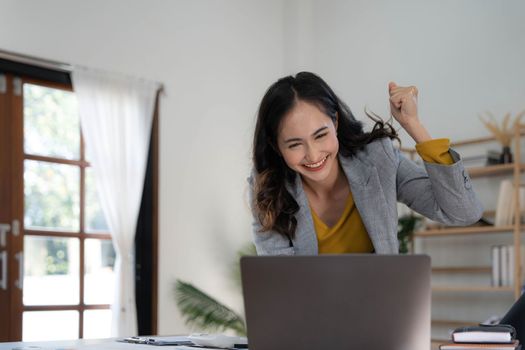 Happy excited asian woman celebrate with computer laptop, success or happy action. Freelancer or Entrepreneur using technology and start up modern home