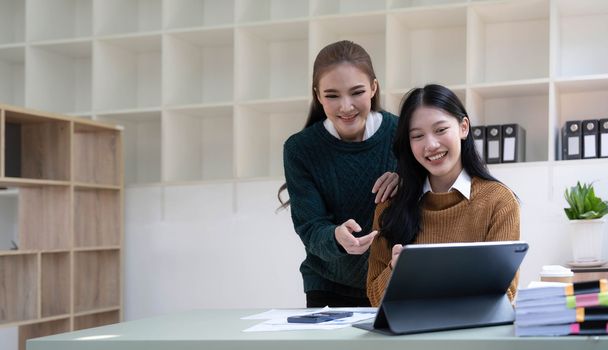 Two young Asian business woman talk, consult, discuss working with new startup project idea presentation analyze plan marketing and investment in the office...