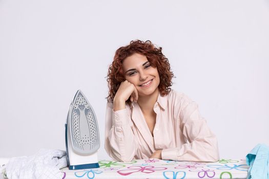 A happy and full of joyful smile girl sits at the ironing board and iron. An eager woman for work.