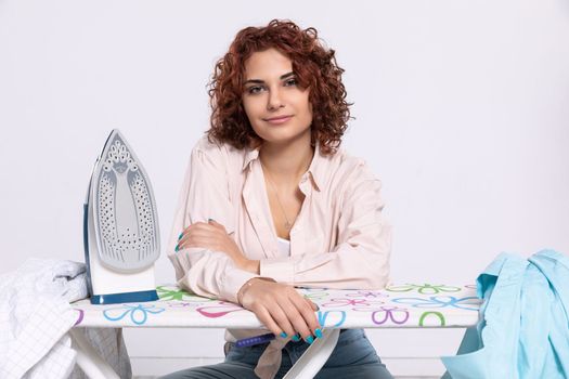 Sitting position on a chair. The girl rests her hands on the ironing board. A young girl will iron men's shirts.