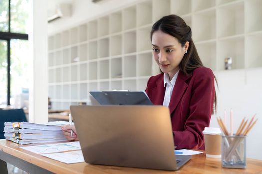 Asian Business woman using calculator and laptop for doing math finance on an office desk, tax, report, accounting, statistics, and analytical research concept.