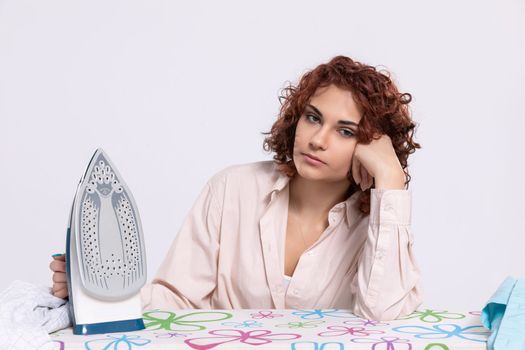 At the ironing board sits a girl, worried and disappointed by the constant ironing of shirts. Monotonous housework.