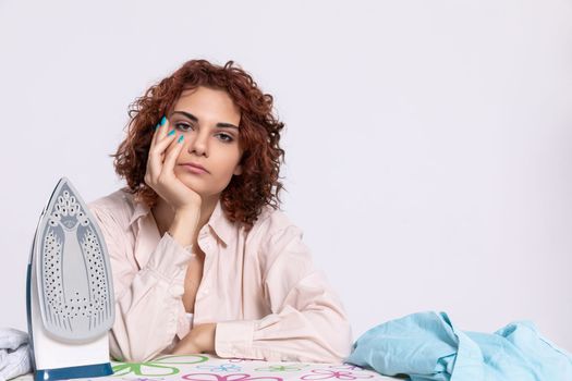At the ironing board sits a girl, worried and disappointed by the constant ironing of shirts. Monotonous housework.