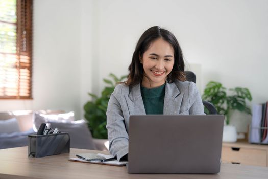 Asian Business woman using calculator and laptop for doing math finance on an office desk, tax, report, accounting, statistics, and analytical research concept..