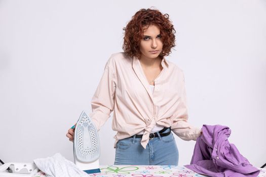 Annoyed woman with the next batch of clothes to iron. She dislikes ironing. Daily housework after washing clothes is ironing shirts.