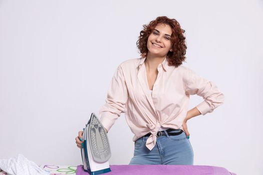 A girl with a smile on her face stands at the ironing board and in her hand holds an iron. Daily household chores.