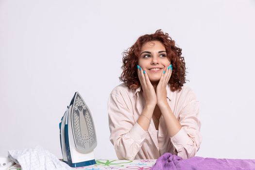 A young girl with curly hair with a smile on her face. A woman full of joy and willingness to work. Ironing board and iron.