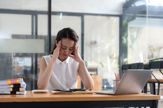 Young Business Asian women are stressed while working on laptop, Tired asian businesswoman with headache at office, feeling sick at work copy space in workplace an home office..