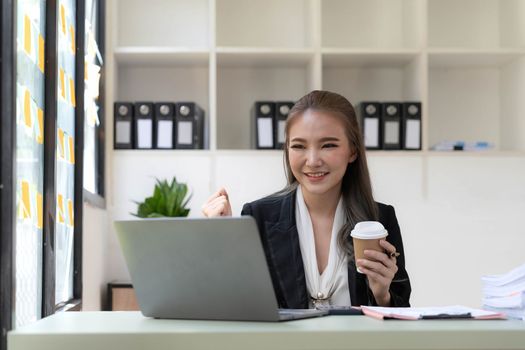 Pretty Asian businesswoman sitting on a laptop And the work came out successfully and the goal was achieved, happy and satisfied with her...