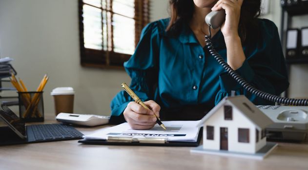 Home loan contract. house model on workplace desk with real estate agent professional making business call talking on phone with customer for signing rental lease contract in office concept.