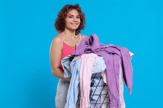A girl with a smile on her face carries a basket full of washed and dried men's shirts. Joy and contentment. Dark curly hair.