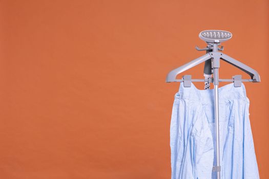 Men's shirt. Hot steam device for ironing clothes with hanger. Uniform brick-colored background. Isolated from the background.