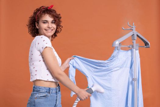 Smiling girl using a steamer to iron a man's shirt. Attractive girl with dark and curly hair. Hot steam.